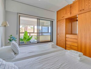 Une chambre d’hôtel dotée d’une grande porte-fenêtre coulissante donnant sur le balcon, d’une armoire en bois et d’un lit agrémenté de serviettes blanches soigneusement pliées.