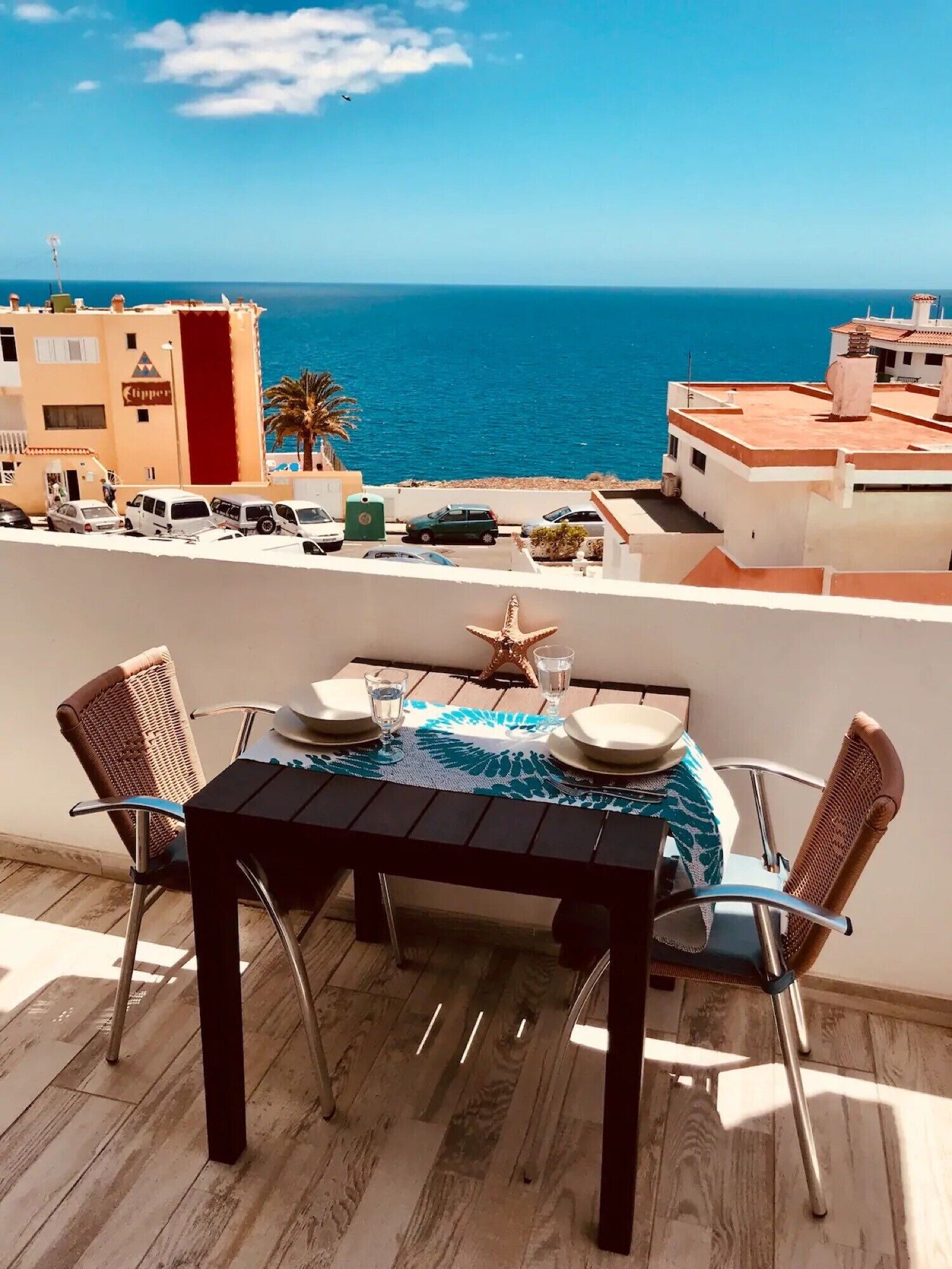 Een balkon met een tafel gedekt voor twee personen, met uitzicht op de kust.