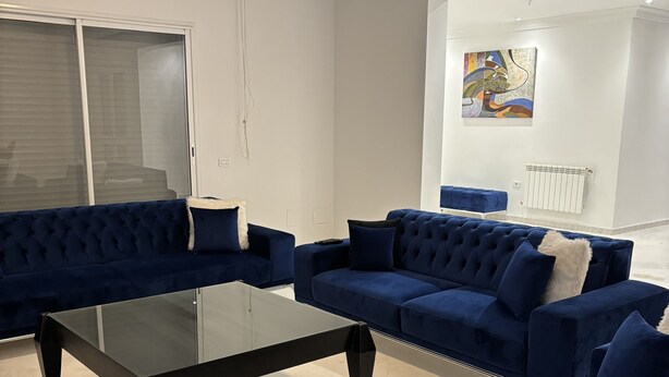 A modern living room with a sectional sofa, a glass coffee table, and a white radiator. - Apparemment Haut Standing 170m (Tunis)