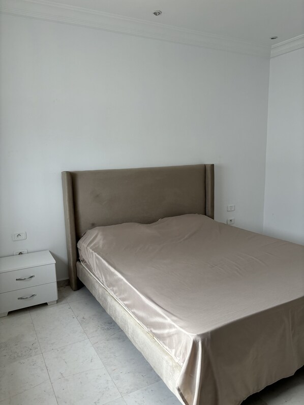 A bedroom with a single bed, a nightstand, and a power outlet on the wall.