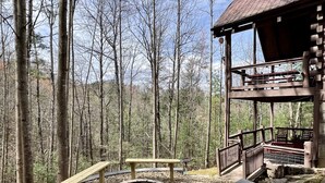 Un chalet rustique doté d’un foyer en pierre et de bancs en bois, entouré d’une forêt.