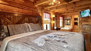 Une chambre dans une cabane en bois, avec un lit, un ventilateur de plafond, une télévision et une pancarte indiquant « RELAX ».