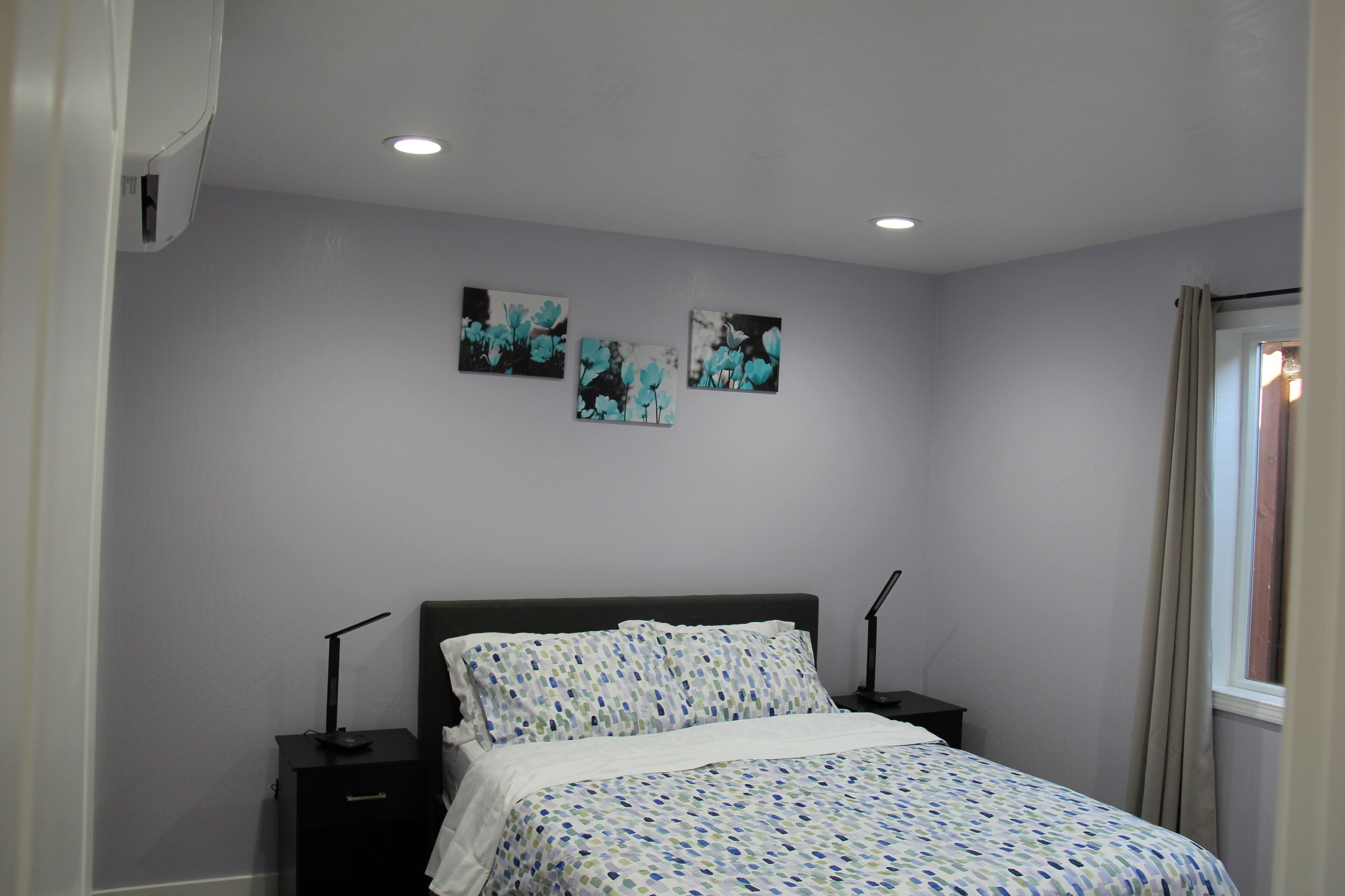 Een slaapkamer met een bed, twee nachtkastjes en drie aan de muur bevestigde foto's.