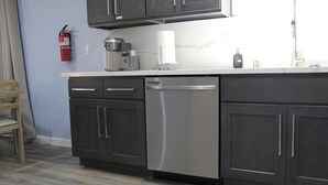 Una cocina moderna con armarios oscuros, lavavajillas de acero inoxidable y encimera blanca.