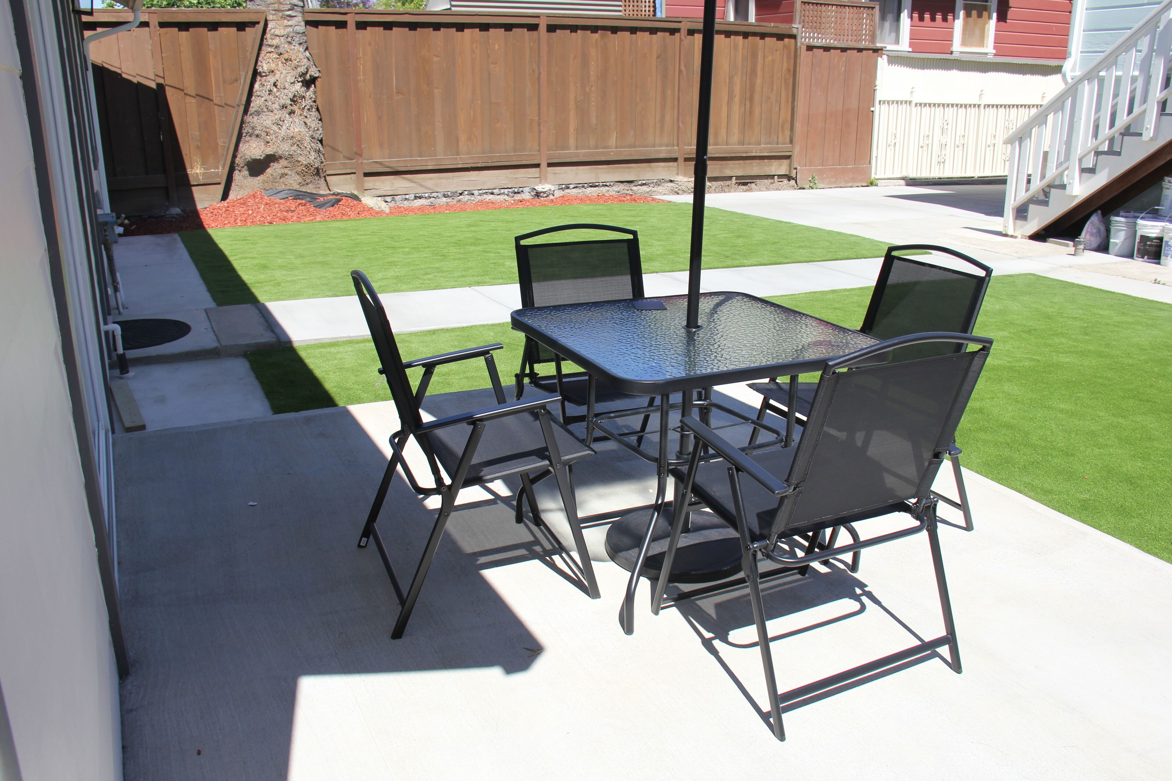 Een terras met een tafel en stoelen, een betonnen vloer en een gazon.