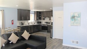 Una cocina moderna con armarios oscuros, un comedor con mesa y sillas, y una sala de estar con un sofá negro.