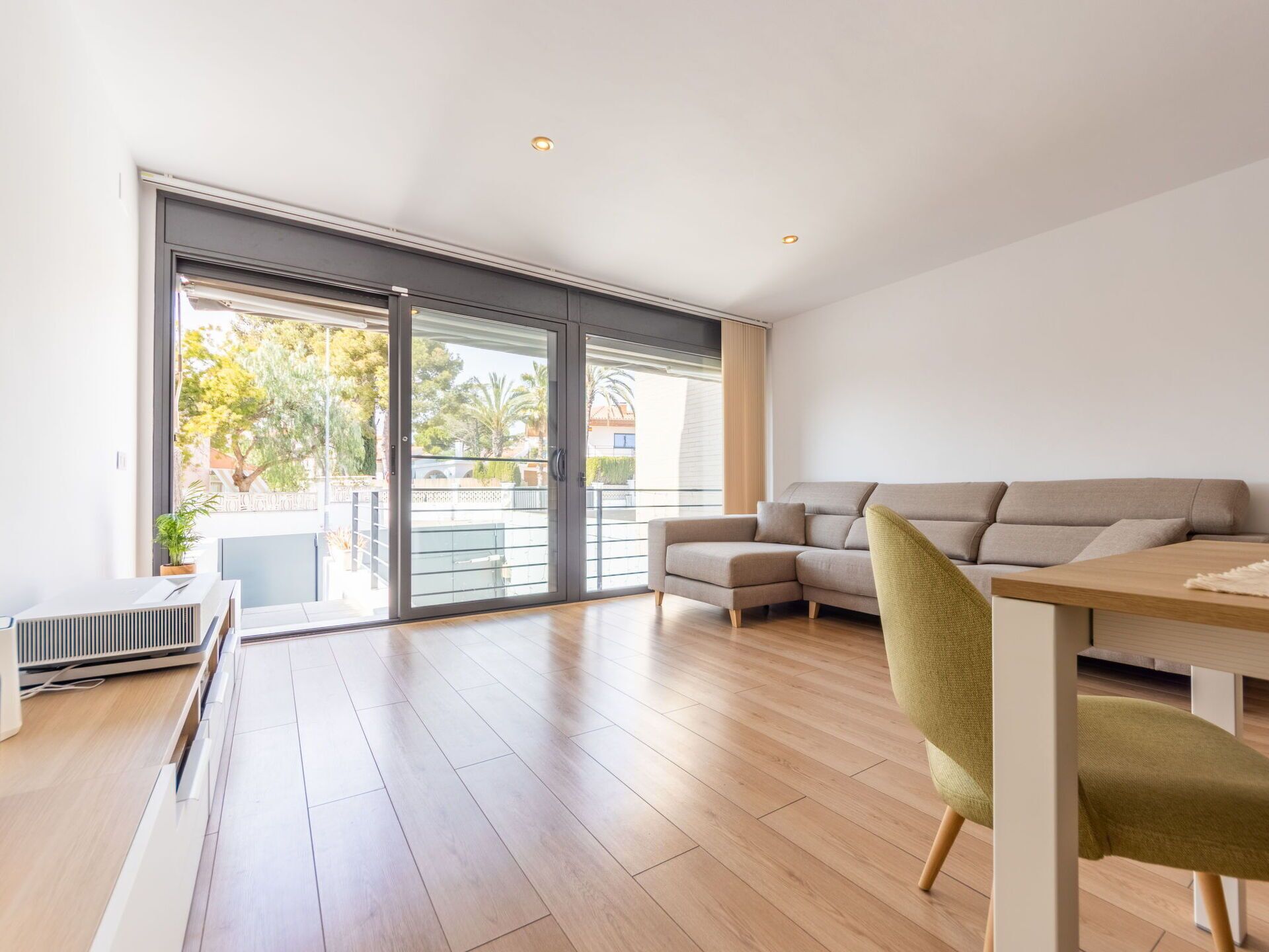 Ein modernes Wohnzimmer mit einer Eckcouch, einem Esstisch und einer Schiebeglasdoor zum Balkon.