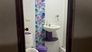 Et badeværelse med toilet, håndvask og en lilla kurv.