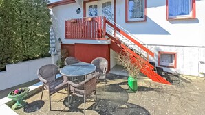 A two-story building with a red exterior and white trim. There is a balcony with wicker furniture and a green vase. A red staircase leads to the upper floor. - Ferienwohnung Bansin (Seebad) (Bansin (Seebad))