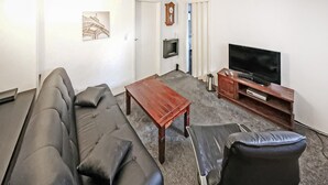 A living room with a sofa, a coffee table, a TV, and a clock on the wall. - Ferienwohnung Bansin (Seebad) (Bansin (Seebad))
