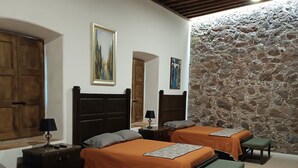 A hotel room with two beds, a stone wall, wooden ceiling beams, and a painting on the wall. - Hotel Hacienda Maravillas (Nopala)