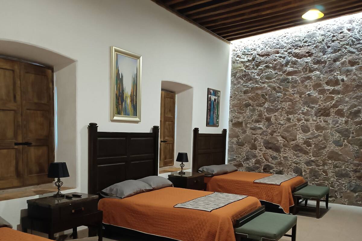Une chambre d’hôtel avec deux lits, un mur en pierre, des poutres en bois au plafond et un tableau accroché au mur.