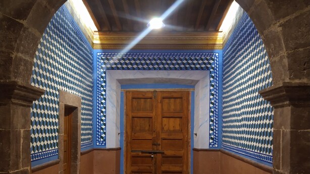 An arched hallway with a patterned blue and white wall, a wooden door, and stone flooring. - Hotel Hacienda Maravillas (Nopala)
