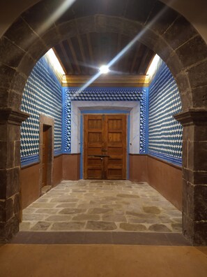 Un couloir voûté avec un mur aux motifs bleus et blancs, une porte en bois et un sol en pierre.