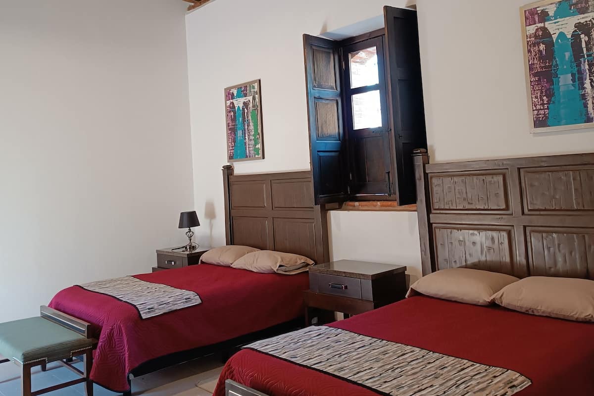 Une chambre avec deux lits, des poutres en bois au plafond, une fenêtre avec vue et un tableau au mur.