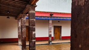 A covered courtyard with stone flooring, wooden columns, and a building with a red and white facade. - Hotel Hacienda Maravillas (Nopala)