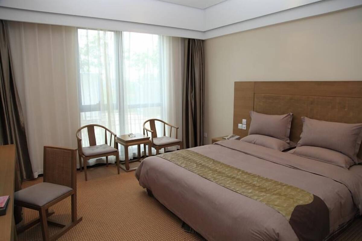 A hotel room with a large bed, two chairs, a small table, and a window with curtains.