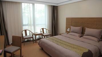 Una habitación de hotel con una cama grande, dos sillas, una mesita y una ventana con cortinas.