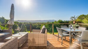 Una terraza con mobiliario de mimbre, una mesa de vidrio y vistas a las montañas.