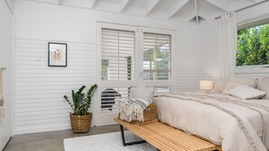 Un dormitorio con cama, mesita de noche, lámpara y ventana con cortinas.