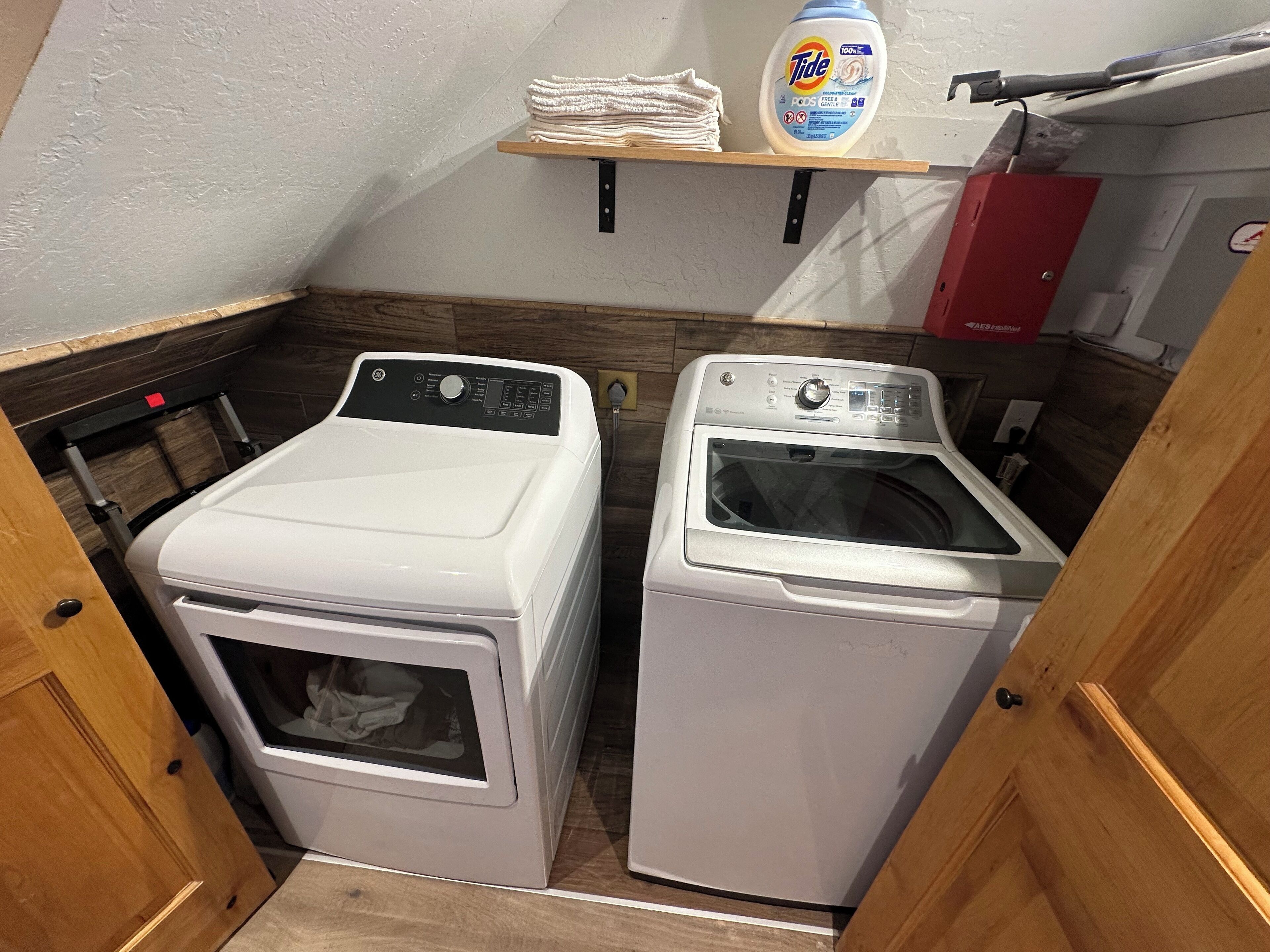 A laundry room with two front-loading washing machines, a shelf with folded towels, and a red cabinet.