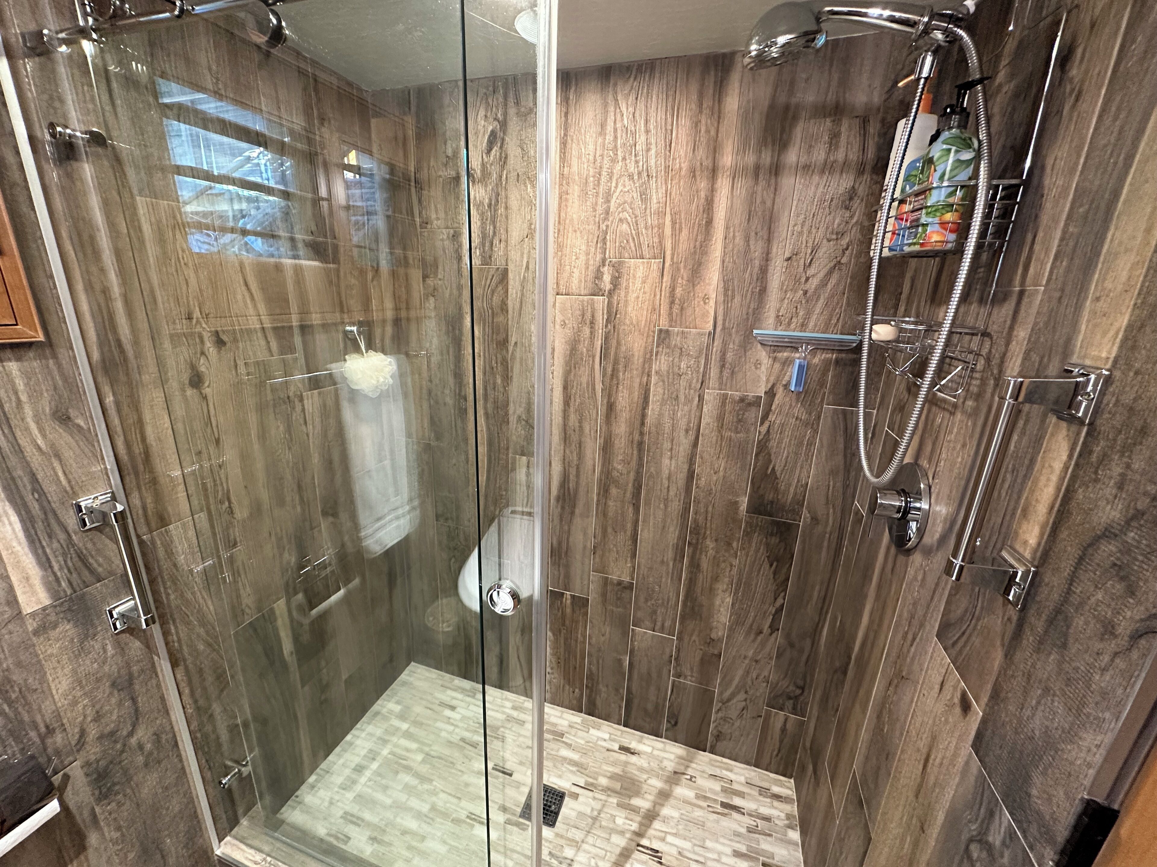 A glass-enclosed shower with wooden paneling, a handheld showerhead, and a handheld shower attachment.