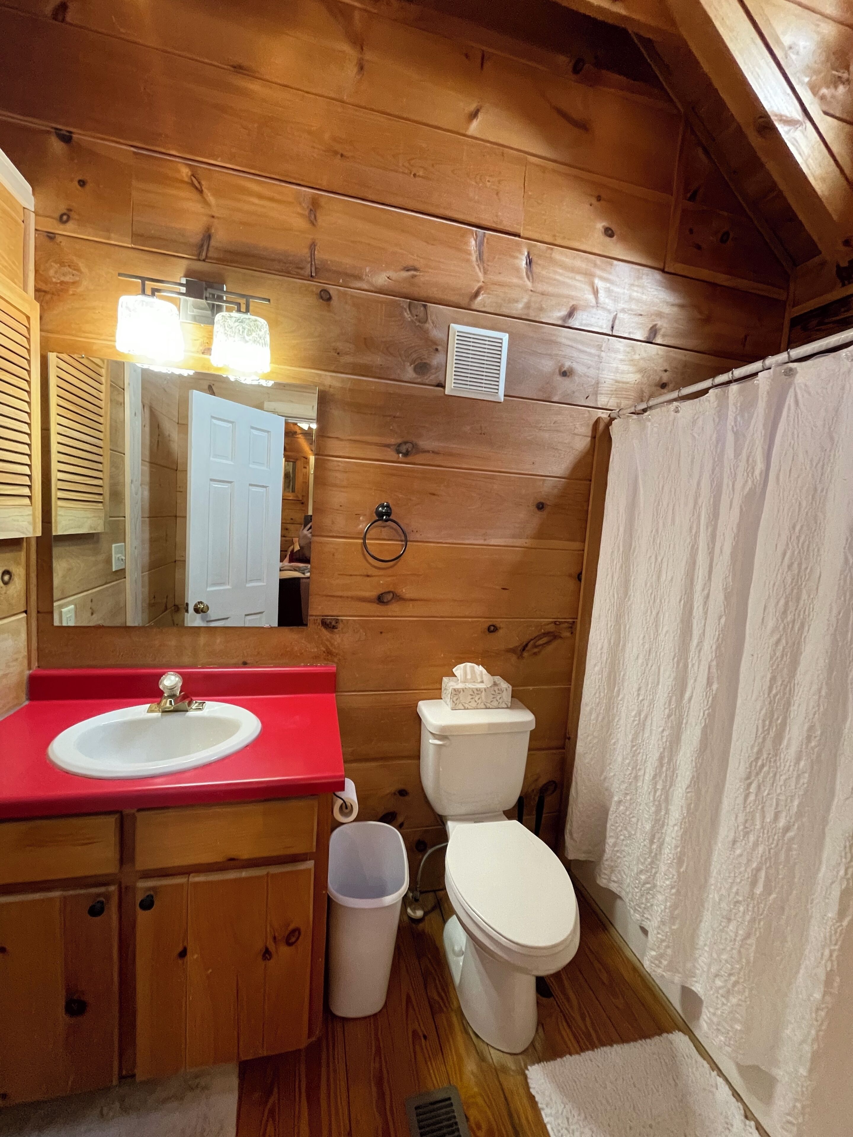 Ein Badezimmer einer Holzhütte mit einem roten Waschbecken, einer weißen Toilette und einer Duschvorhang.