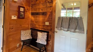 A wooden cabin interior with a bench, a door with curtains, a window, and a thermostat. - Restoration Station: Where Landrum's past Inspires Renewal - 2Bed/2Ba Log Cabin (Landrum)