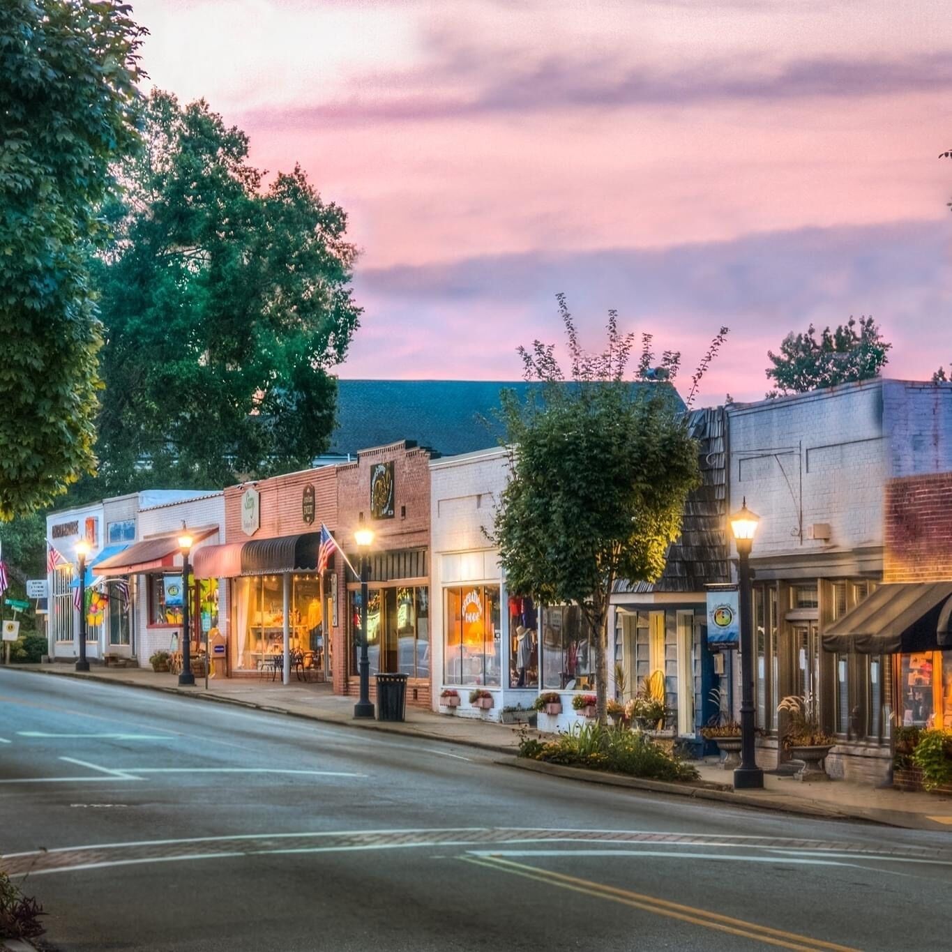 A street lined with small, historic buildings with storefronts, some with awnings and outdoor seating visible.