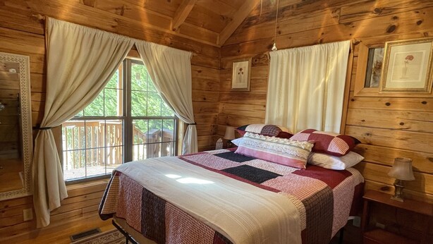 A wooden cabin bedroom with a bed, curtains, a ceiling fan, and a window. - Restoration Station: Where Landrum's past Inspires Renewal - 2Bed/2Ba Log Cabin (Landrum)