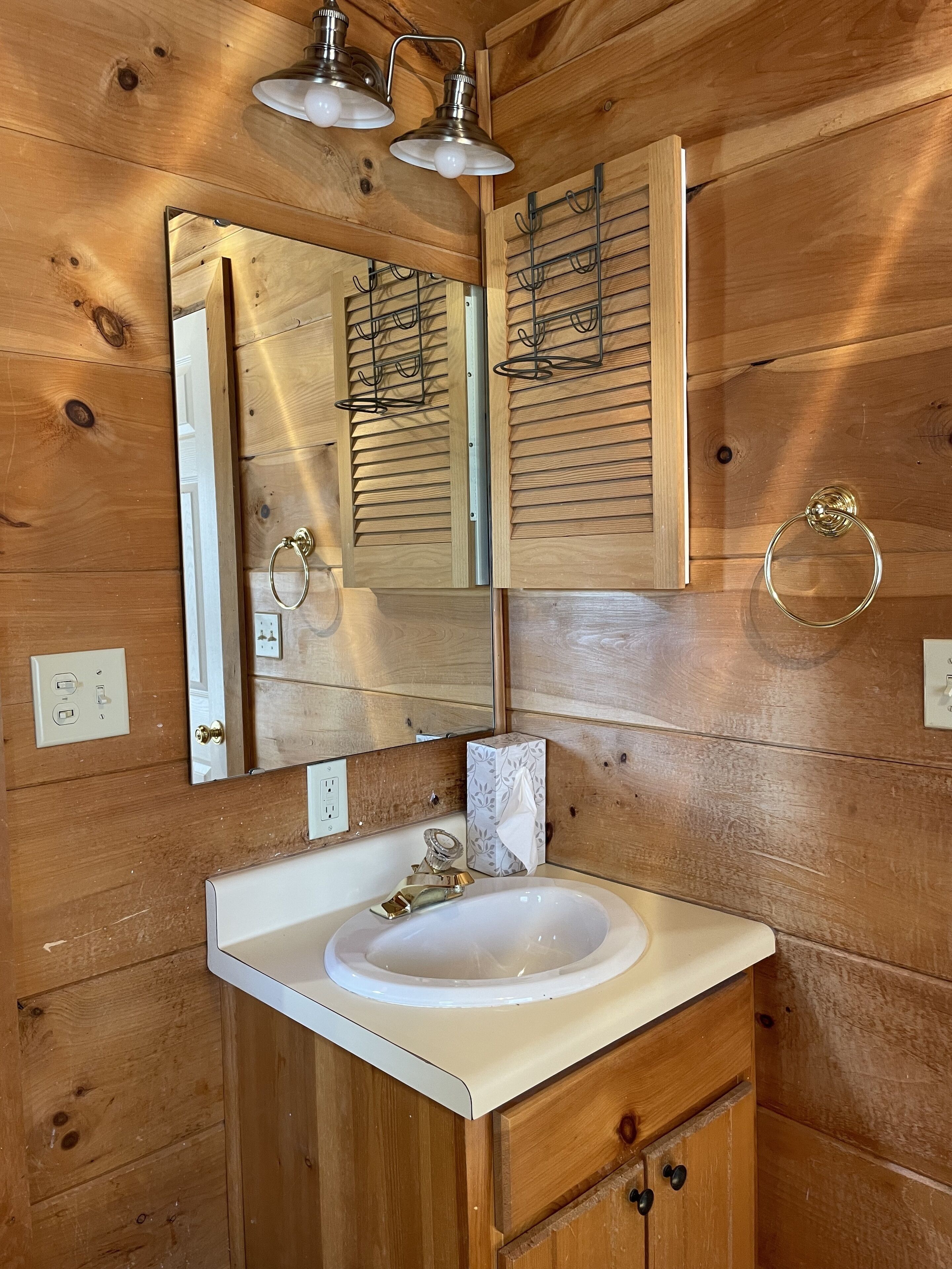 A wooden-paneled bathroom with a white sink, a mirror, and two wall-mounted lights.
