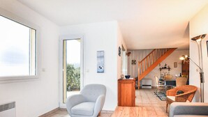 A spacious living area with a large window, a grey armchair, a wooden coffee table, and a staircase leading to a dining area. - Amazing home in Saint Pierre La Mer with WiFi (Saint Pierre La Mer)