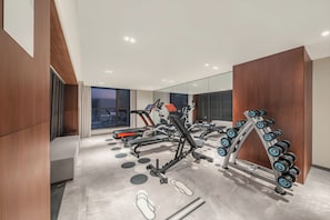 Uma academia moderna com equipamentos de ginástica, um espelho e vista para a cidade ao entardecer.