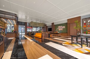A spacious lobby with a black and white marble floor, a wooden reception desk, and a seating area with an orange sofa.