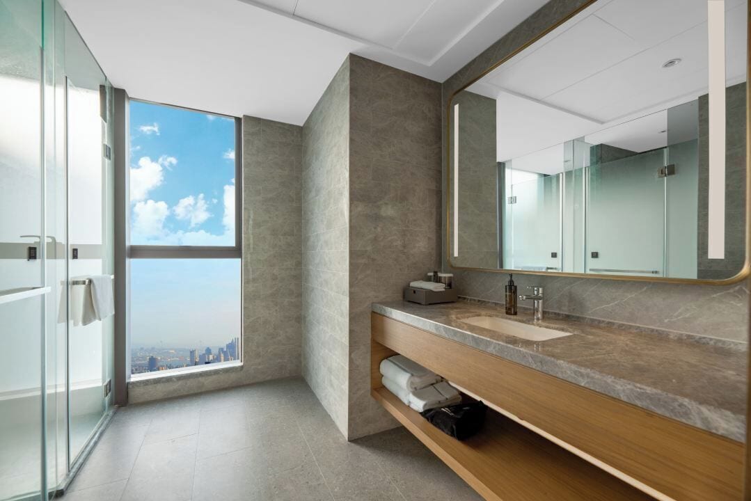 Un baño moderno con un ventanal grande, un tocador con espejo y vistas a la ciudad.