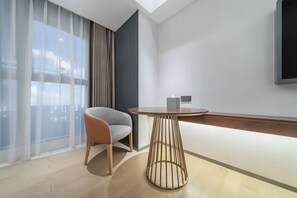 Une chambre moderne avec une table ronde, une chaise, une grande fenêtre avec des rideaux légers et un téléviseur fixé au mur.