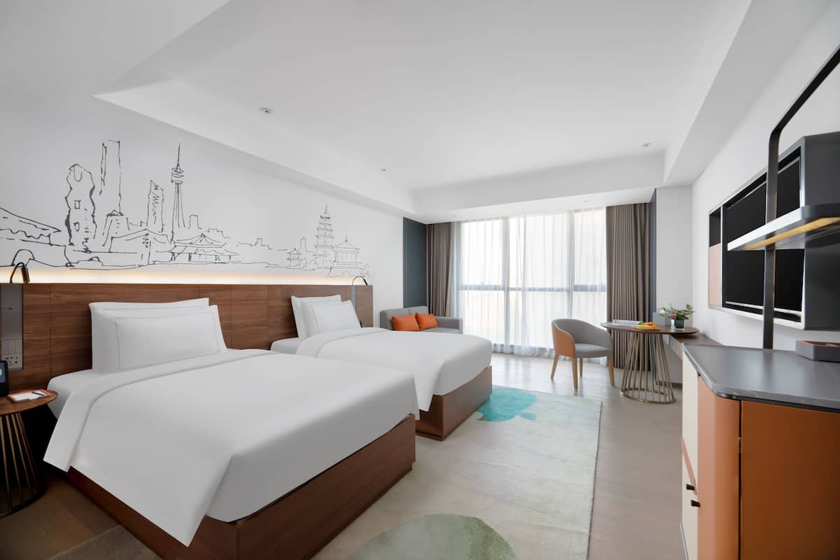 Een hotelkamer met twee bedden, een bureau, een televisie en een stadsgezicht muurschildering.