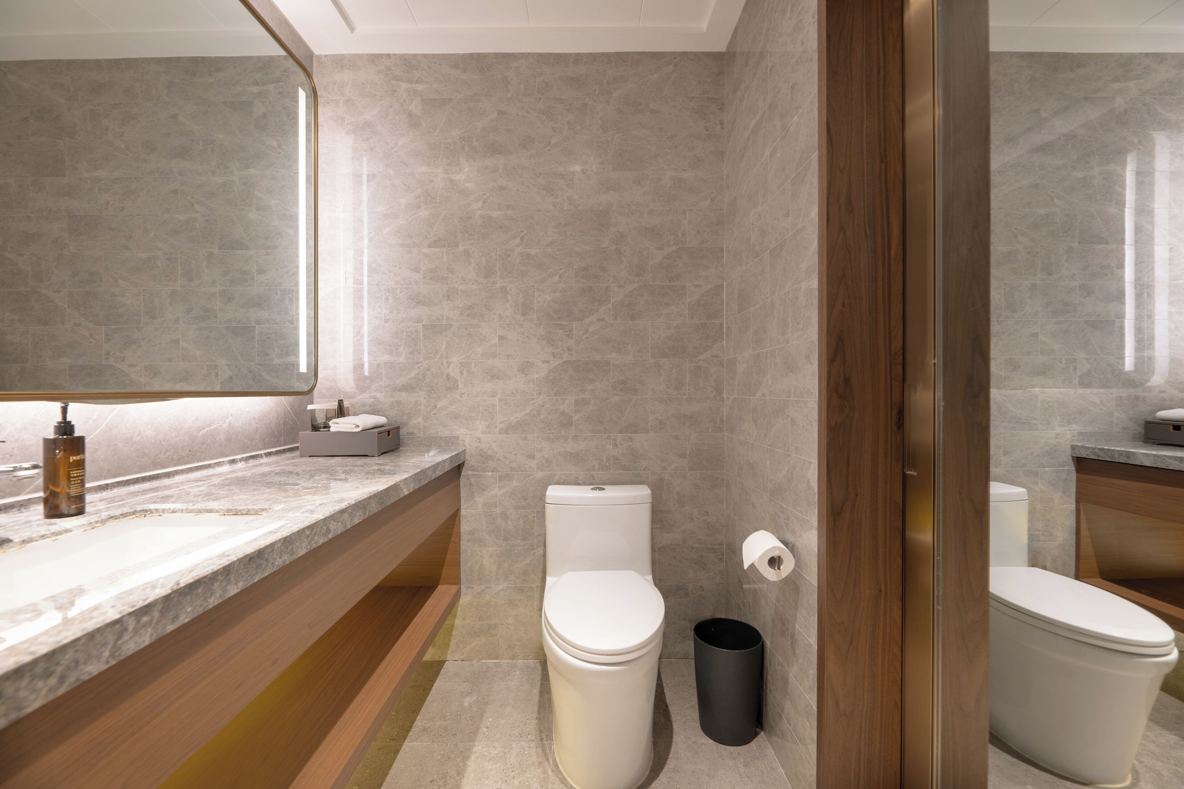 Une salle de bain moderne avec un plan de toilette en marbre, des toilettes, une poubelle et une porte en bois.