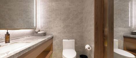 Une salle de bain moderne avec un plan de toilette en marbre, des toilettes, une poubelle et une porte en bois.