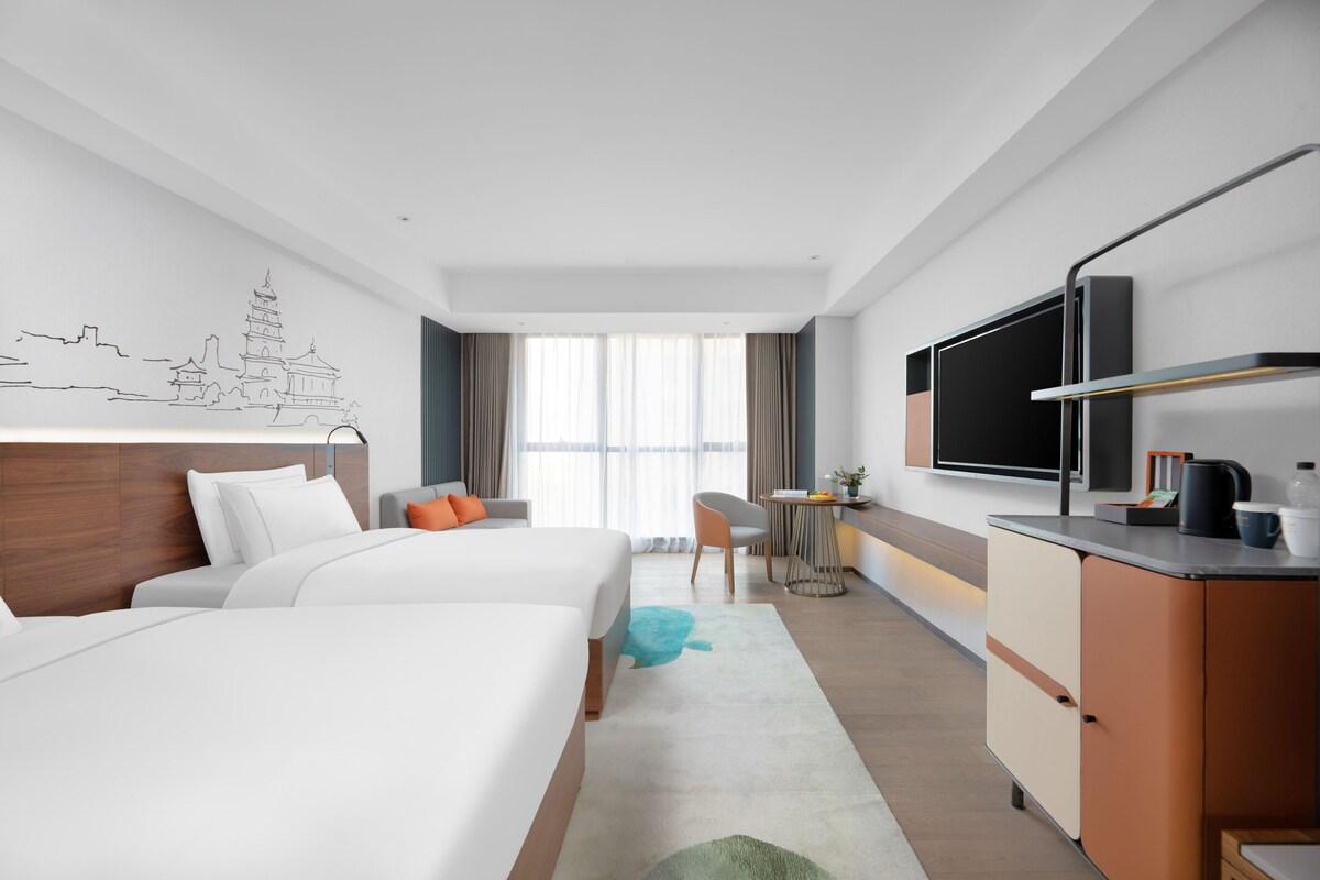 Een hotelkamer met twee bedden, een bureau, een televisie en een wanddecoratie.