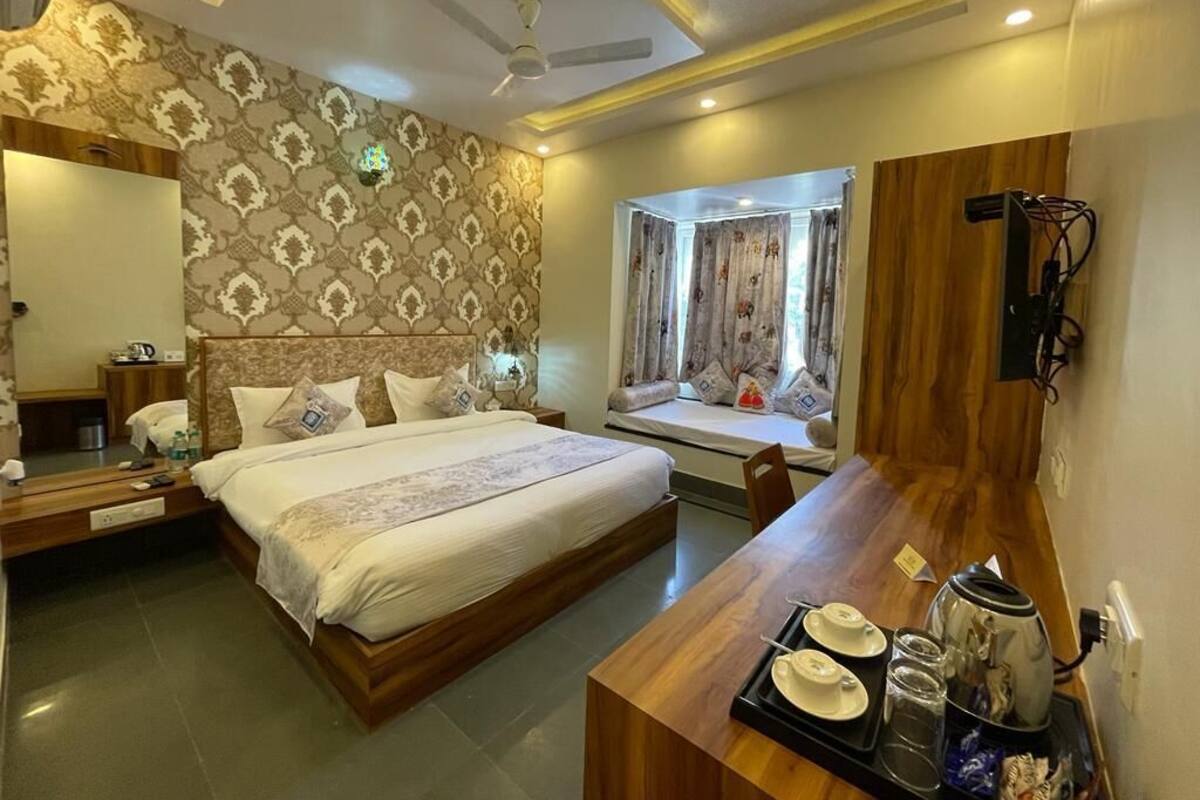 Une chambre d’hôtel avec un grand lit, un bureau en bois sur lequel se trouve un plateau avec des articles pour le petit-déjeuner, une fenêtre avec des rideaux et un ventilateur de plafond.