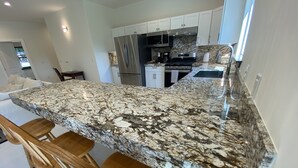 Una cocina moderna con encimera de granito, electrodomésticos de acero inoxidable y taburetes de madera.