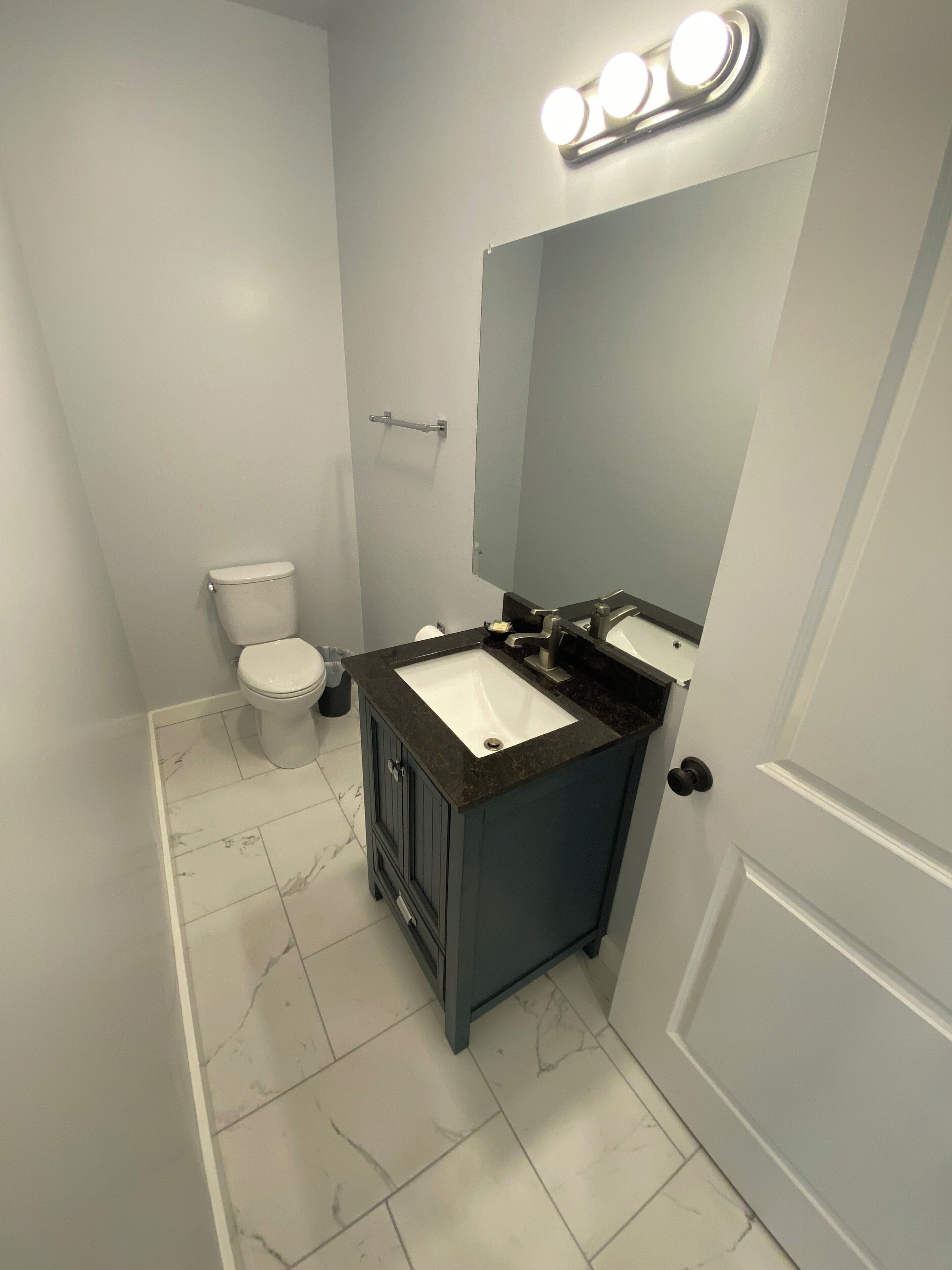 A compact bathroom with a white toilet, a dark sink vanity, and a mirror above the sink.