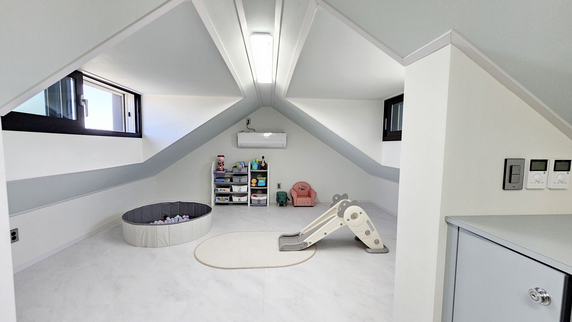 A small, triangular attic bedroom with a bunk bed, a play area, and a storage unit.