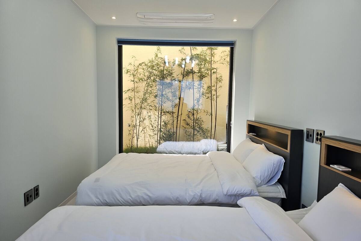 Une chambre d’hôtel moderne avec deux lits, une grande fenêtre donnant sur une bambouseraie et des étagères intégrées.