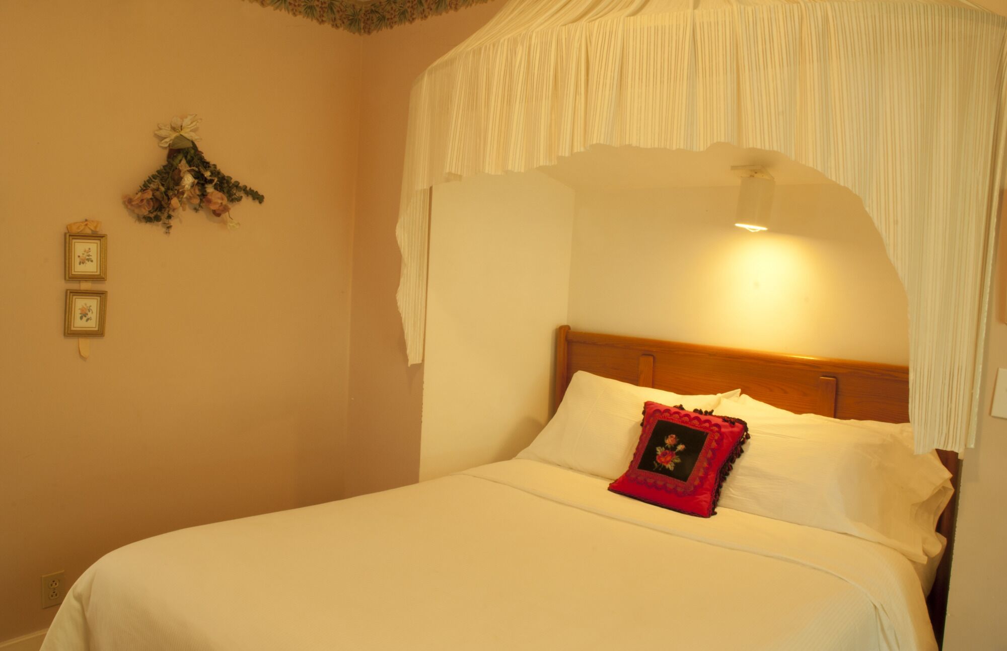 A neatly made bed with white linens and a red pillow, a wooden headboard, and a wall-mounted decoration.