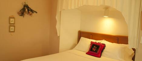 A neatly made bed with white linens and a red pillow, a wooden headboard, and a wall-mounted decoration.