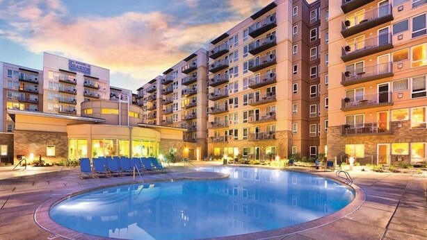Un hotel con piscina rodeada de sillones de descanso y un edificio con varios balcones.