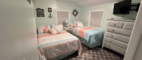 Une chambre avec deux lits, une commode, un téléviseur et un tapis à motifs.
