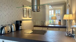 A modern kitchen with a stainless steel range hood, a glass shelf, and a window with a view of a brick building. - Beachhouse Seaside 3 - Beachhouse Seaside 3 Rantum, 107qm mit 3 Schlafzimmern für bis zu 6 Personen (Sylt)